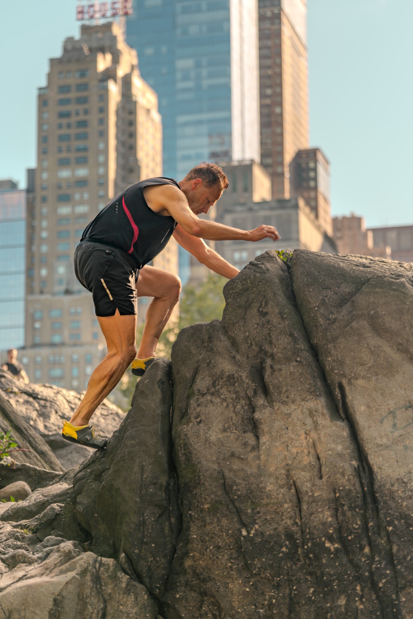 Chuck Garcia climbing a large boulder with city high-rises behind him.